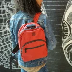 A man carrying the Red Smell Proof Backpack over one shoulder